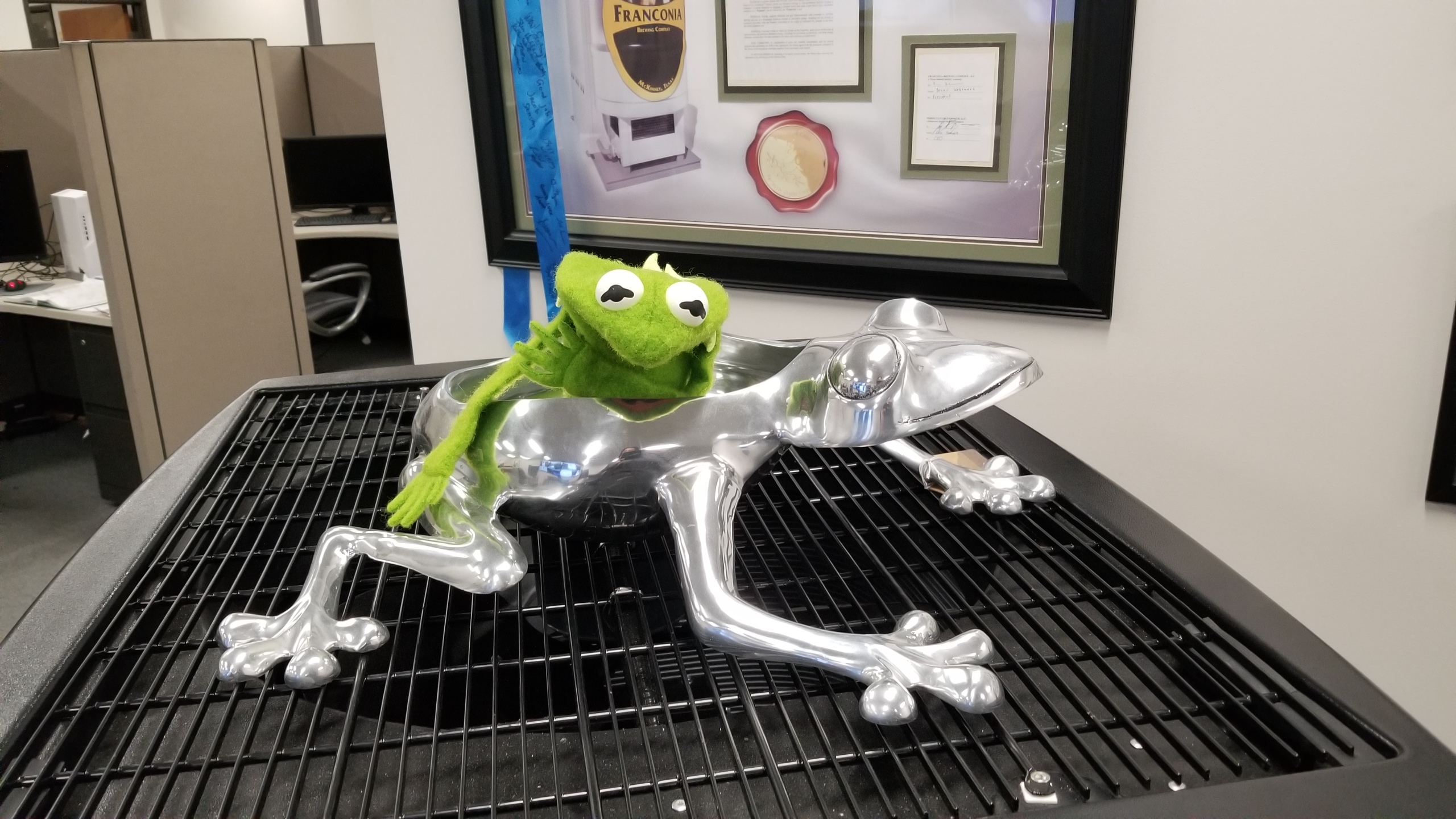 Green frog figure inside a polished metal frog sculpture in the Perfectly Green office